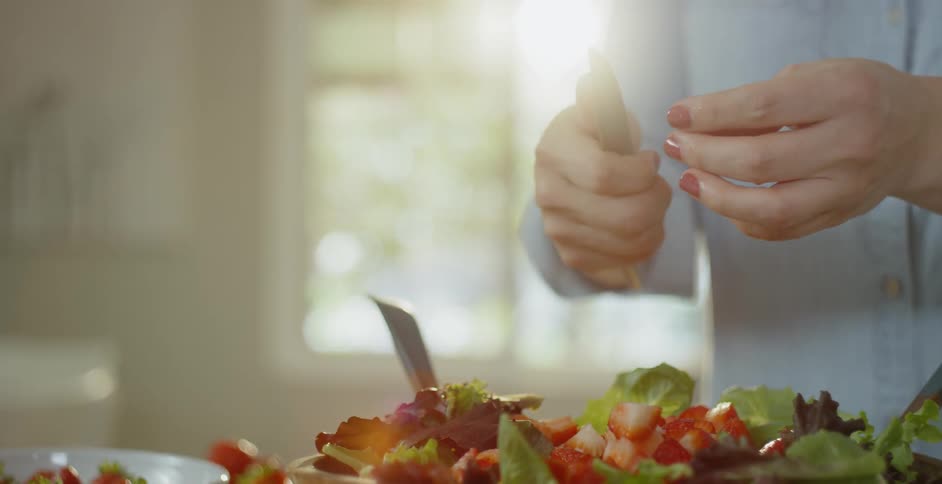 A woman is slicing strawberries for a salad in a kitchen in daylight