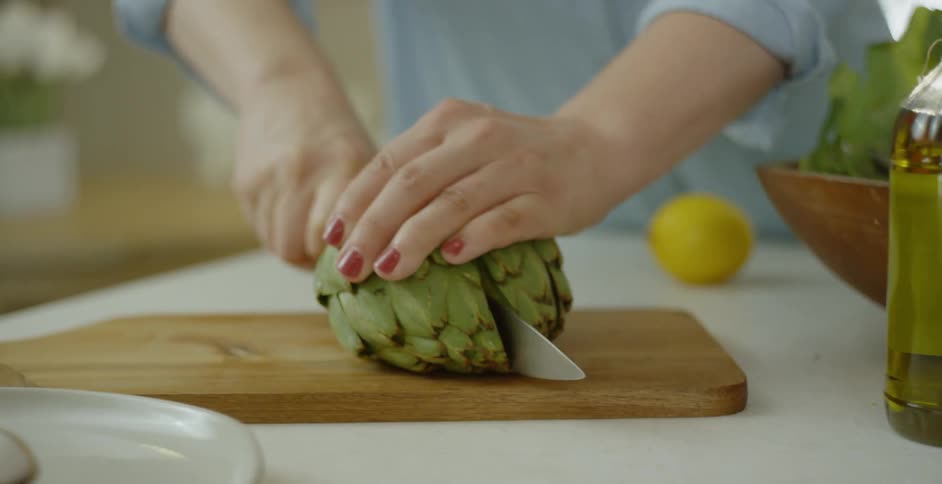 A woman is slicing an artichoke in half in daylight