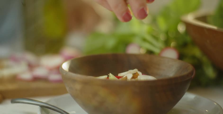 A woman is dropping chopped nuts into a salad bowl