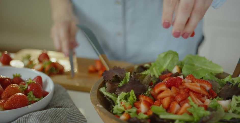 Person cuts strawberries and put them in a salad