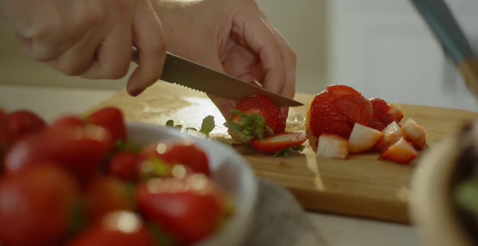 A person cuts up the strawberries on the cutting board