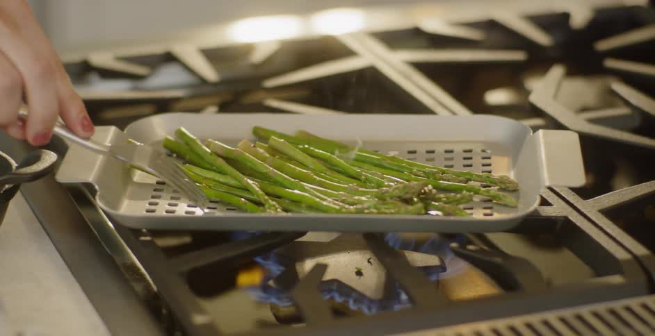 A woman is grilling asparagus on a stovetop in a kitchen during the day