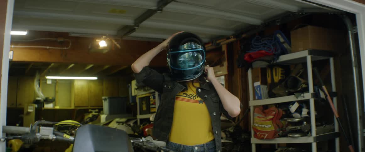A woman carries a motorcycle helmet and puts it on
