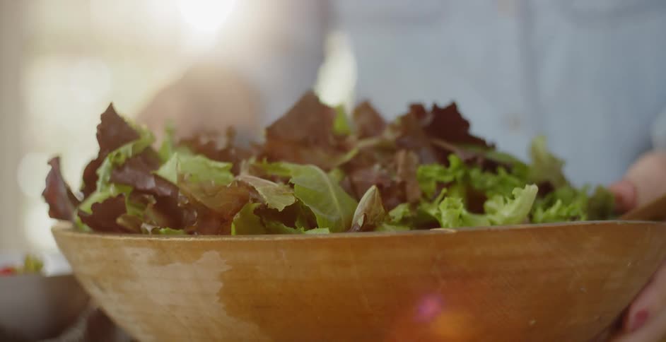 A woman prepares a salad in a wood bowl