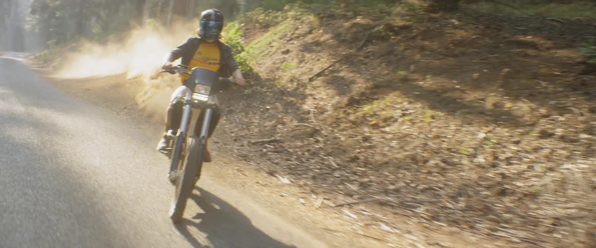 A woman is riding a motorcycle on a road and embankment in a forest in daylight