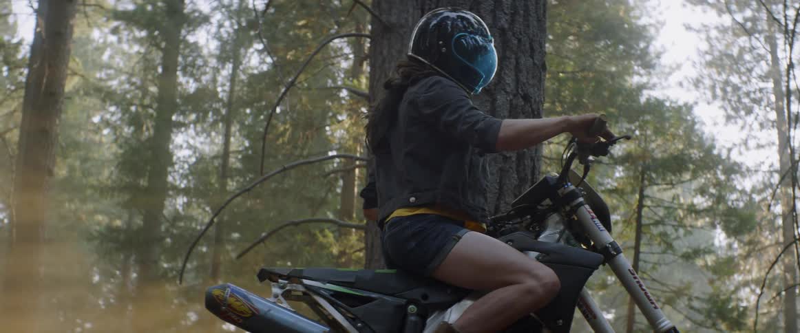 Woman wearing a helmet sits on a motorcycle in the woods