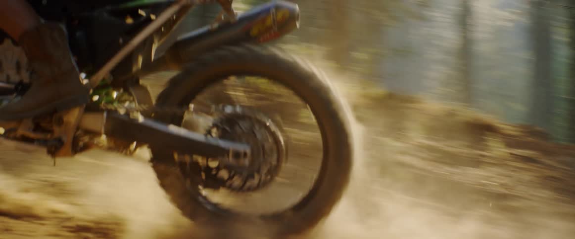 A woman rides a dirt bike on a forest trail