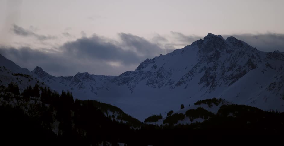 Clouds pass behind a snowy mountain peak