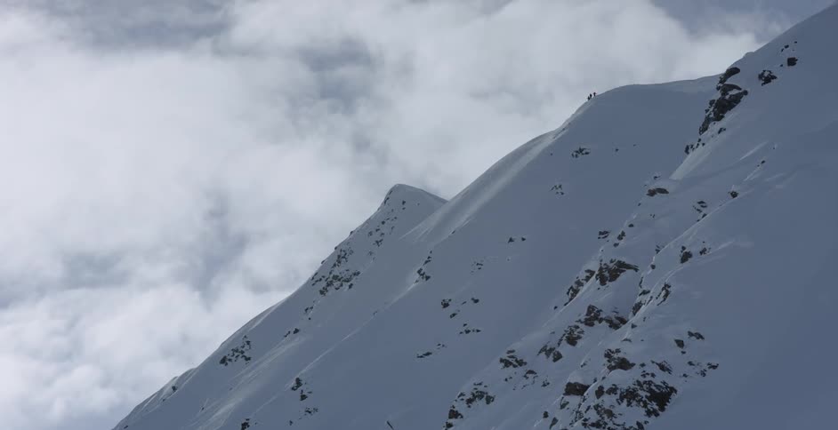 Hikers summit a snow covered mountain in the clouds