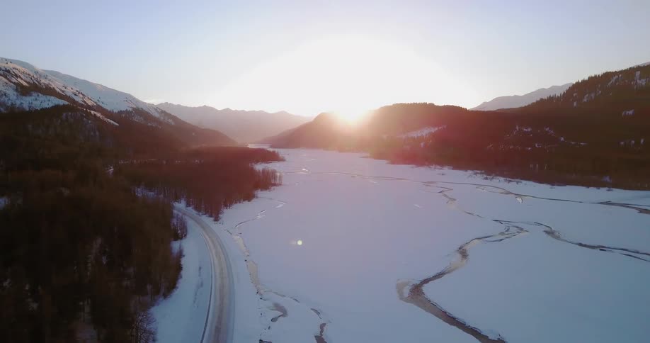 The sun sets behind mountains with snow on the ground