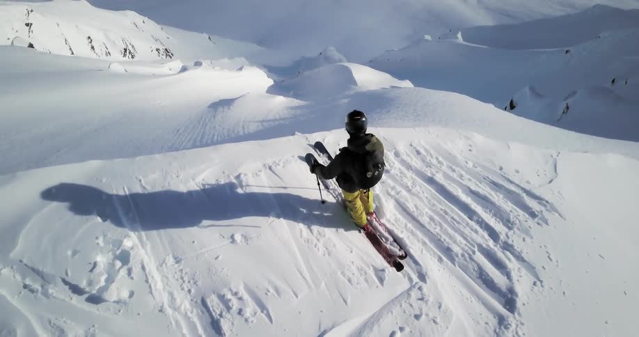 A skier is standing at the top of a large mountain looking down