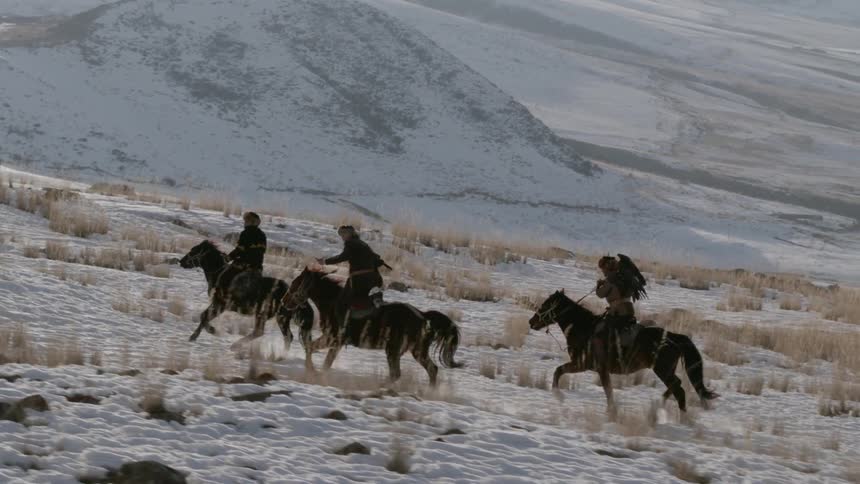Three people ride horses on the snow covered hills