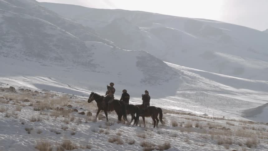 Three people ride horses on the snow covered hills