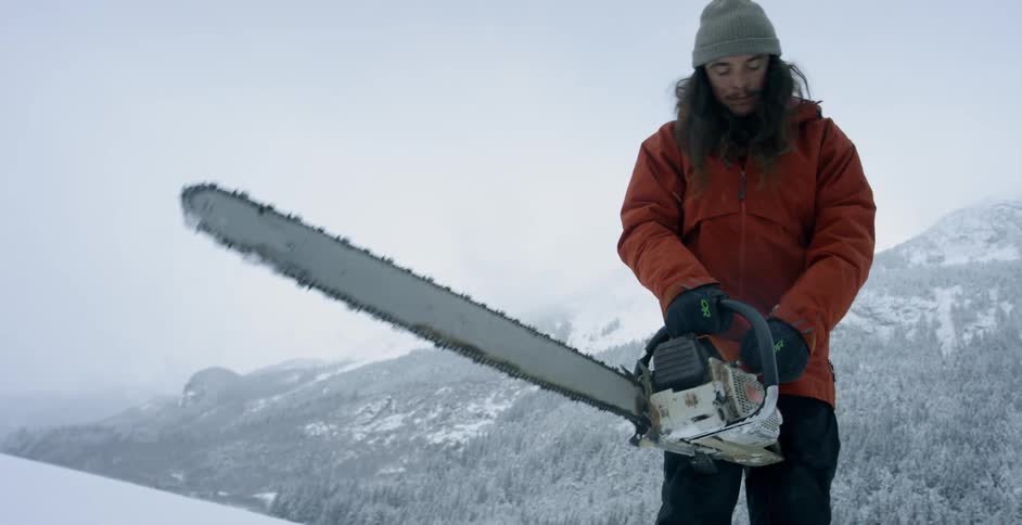 A man struggles to start a chainsaw in the snow