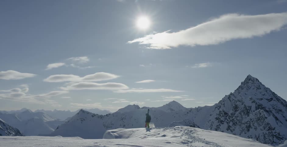 A skier is standing on a snowy mountain peak on a sunny day