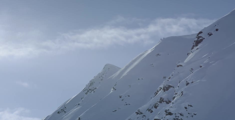 Distant climbers reach the peak of a snow covered mountain