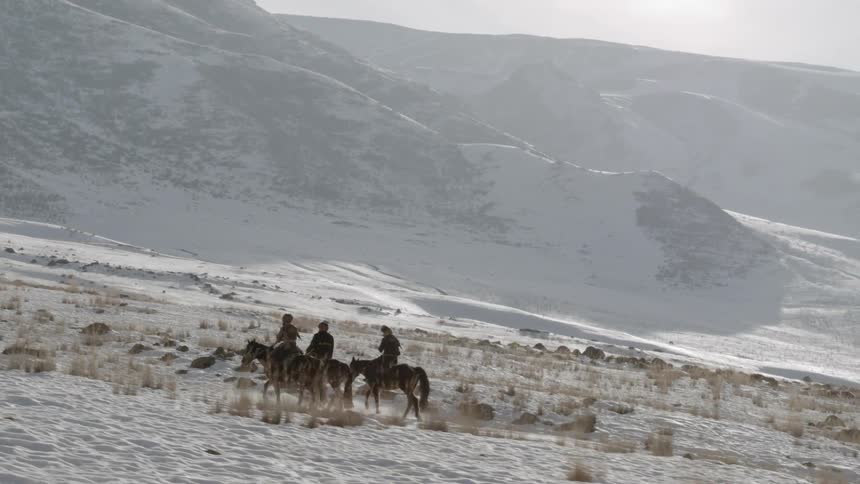 Three people are riding horses on a mountainside on a winter day