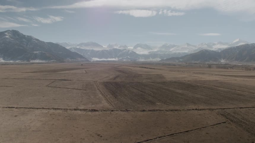 Barren flatland leads to snow capped hills and peaks