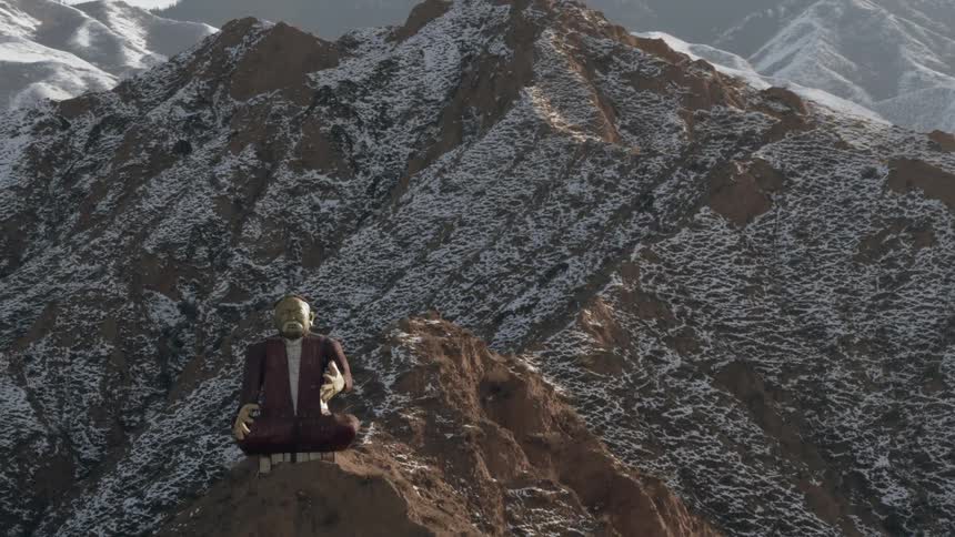 A statue of a man sitting cross legged sits on top of a mountain
