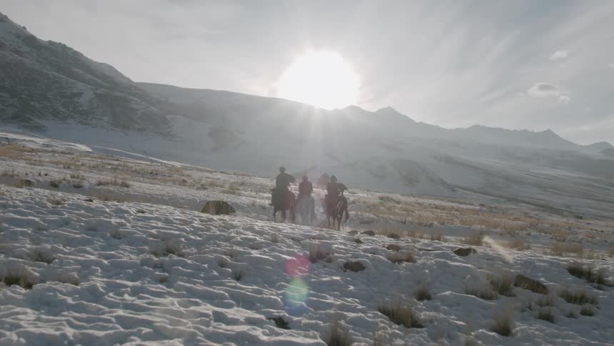 Men on horseback ride across snow covered valley