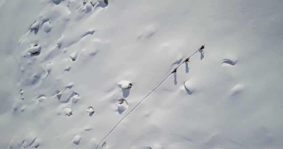3 people are walking in a straight line up a snow covered mountain