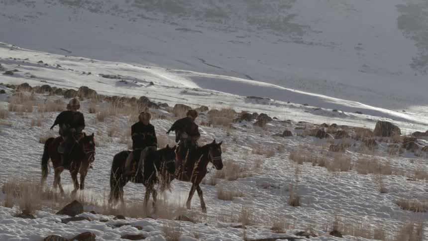 People ride horses across a snowy landscape