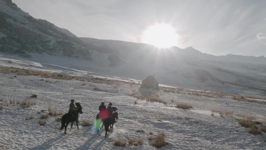 People are travelling on horses across a frozen landscape