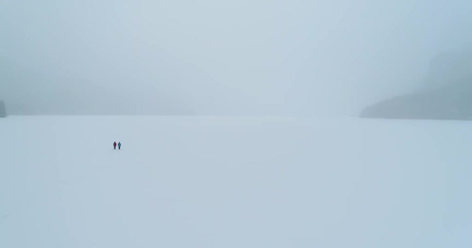 Two people are walking across a frozen lake on a foggy winter day