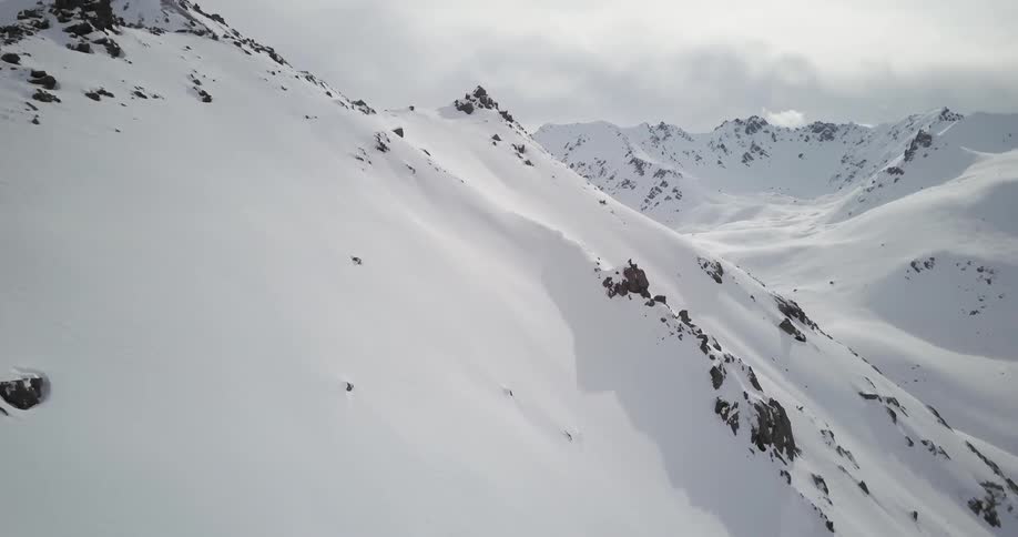 Clouds are lingering over a snow-covered mountain range during the day