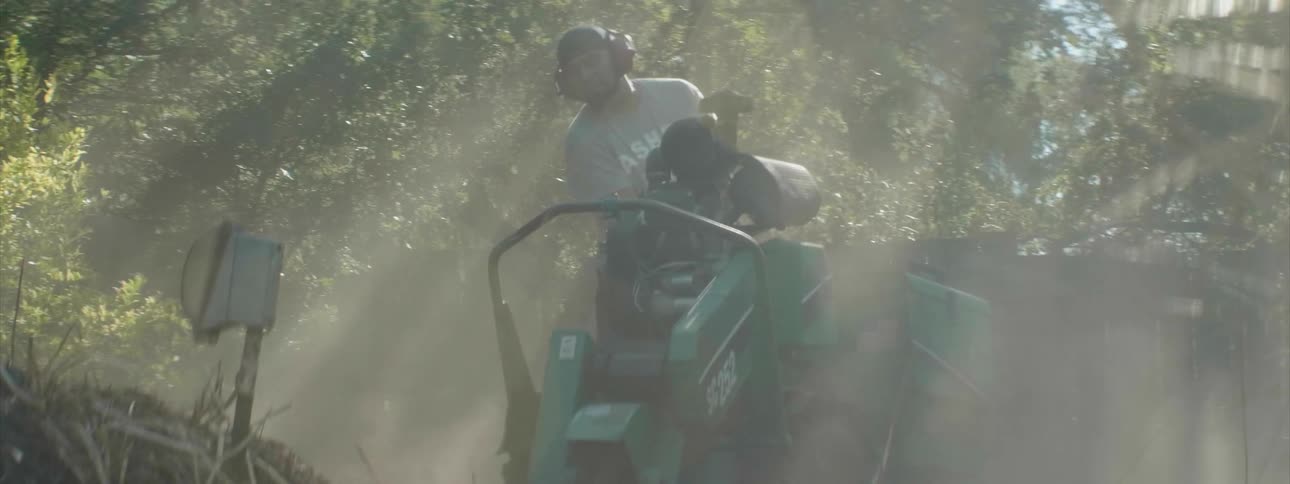Man uses a large machine near trees on a sunny day