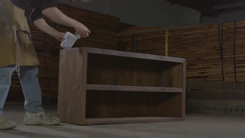 A worker at a furniture factory polishes a wooden bookshelf