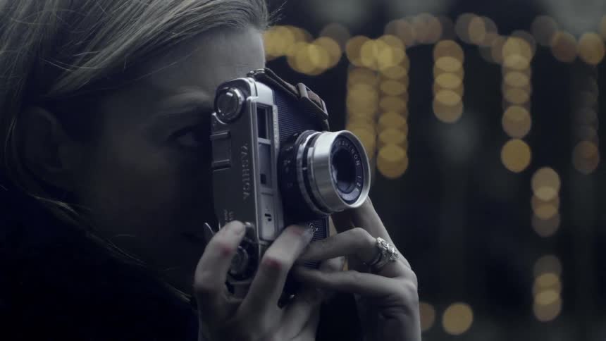 A woman is holding a camera to her eyes as she take pictures at dusk