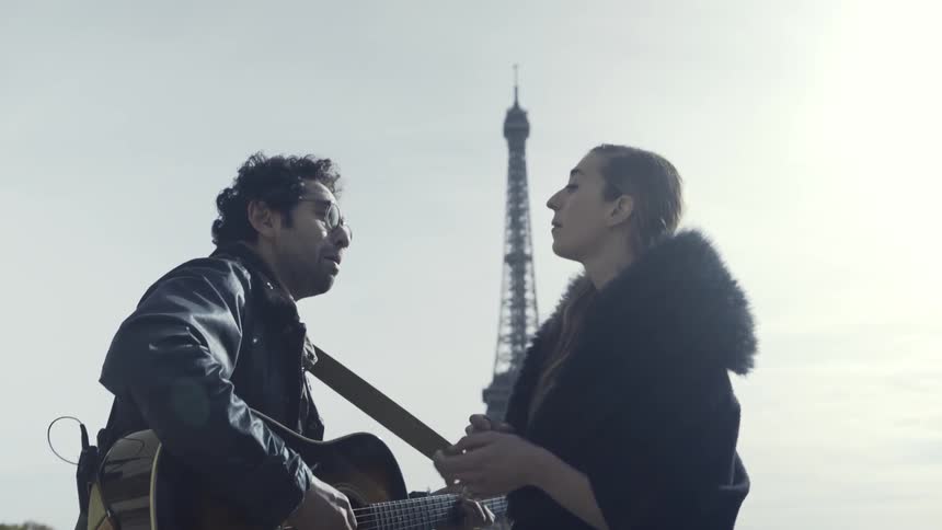 A man and woman play guitar and sing in front of the eiffel tower
