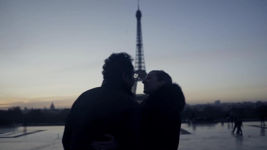 A man and woman kiss in front of the eiffel tower