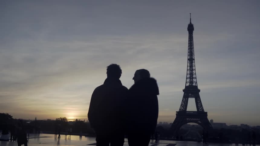 A man and woman are standing and looking at the eiffel tower at dusk