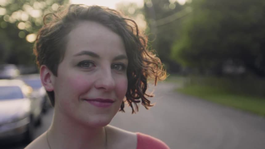 A woman is standing in the street smiling on a sunny day
