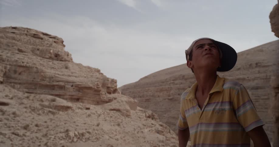 A boy wearing a ball cap looks up at the rock formations
