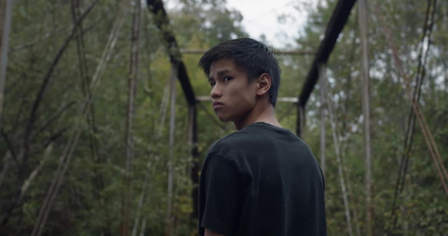 A young man stands on a bridge in the woods