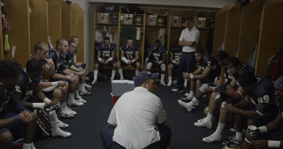 A coach talks to a football team in a locker room