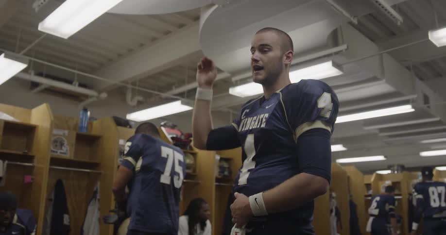 Football player talking and gesturing in a locker room as other players are around