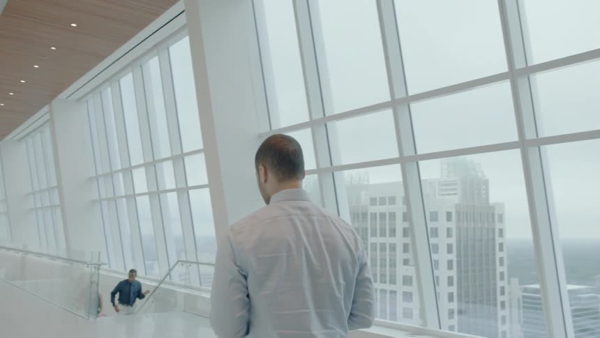 A man in a city office walks along a wall of windows