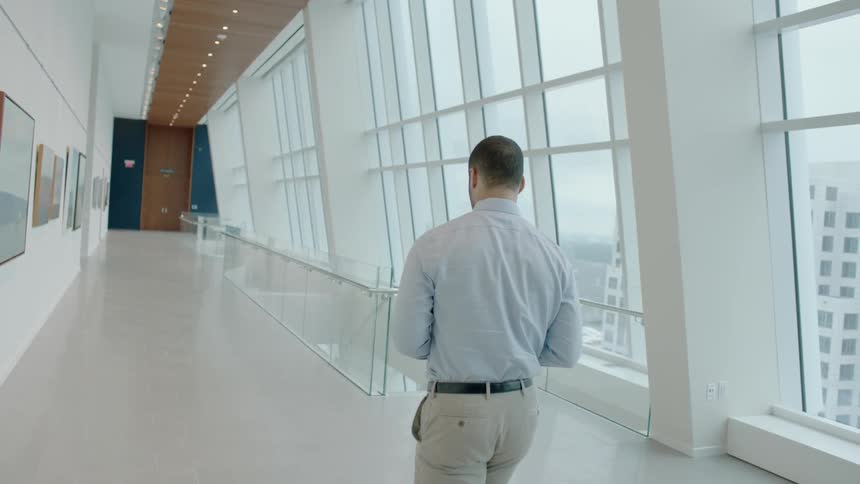 A man is walking in a hallway in an office building during the day