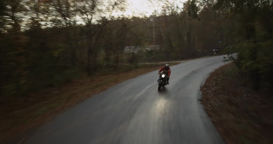 A motorcyclist rides down a narrow rural road
