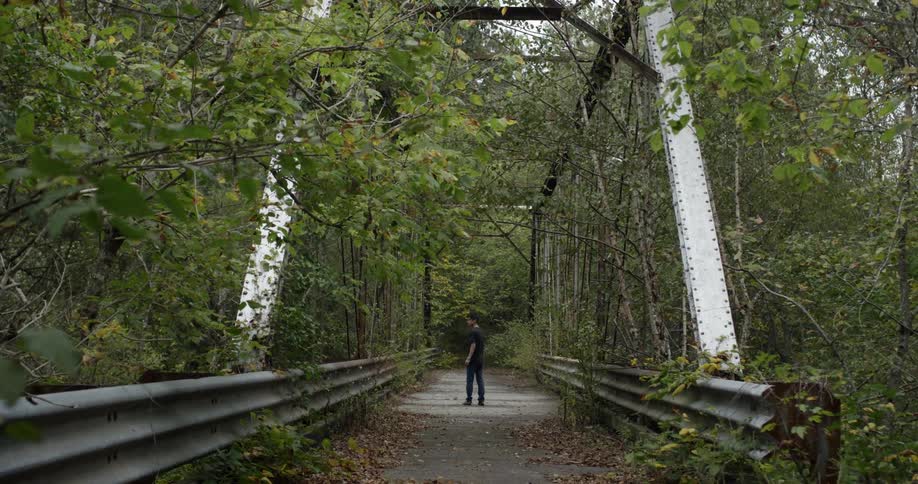 A man is standing on an old bridge and looking behind himself during the day