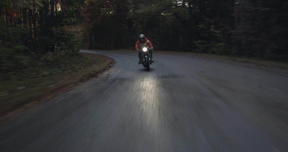 A motorcyclist rides through a forest at sunset