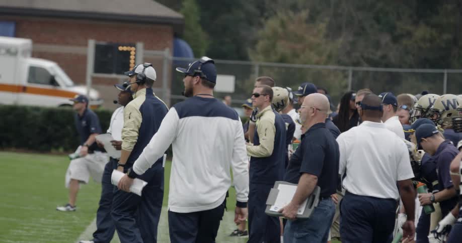 Coaches walk onto the field from the sidelines of a football game