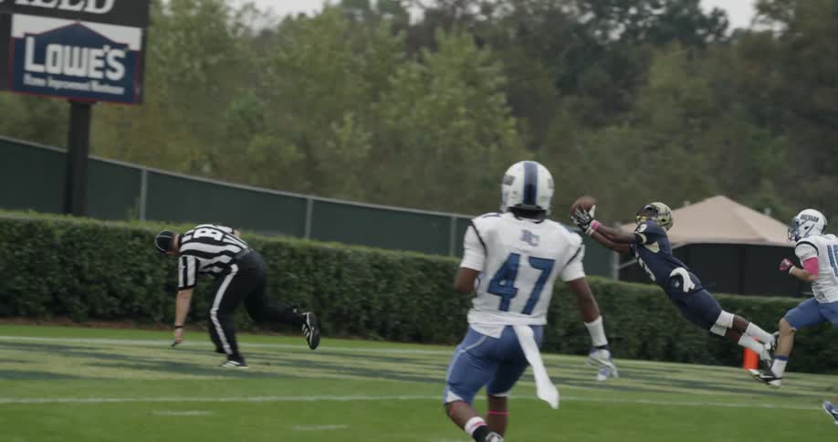A football player is catching a touchdown in a game during the day
