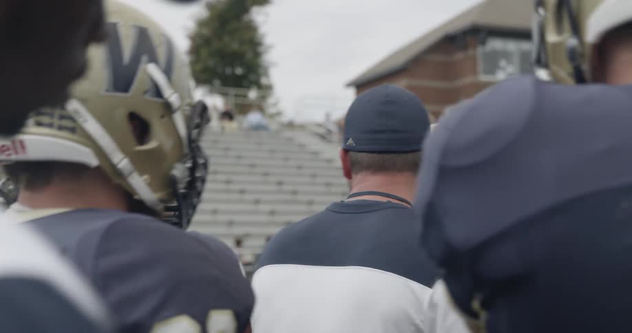 Players surround the football coach as he shouts instruction