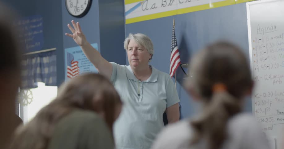A teacher raises her hand as she talks in front of the class