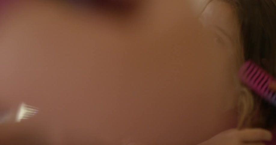A little girl is brushing her hair using a mirror